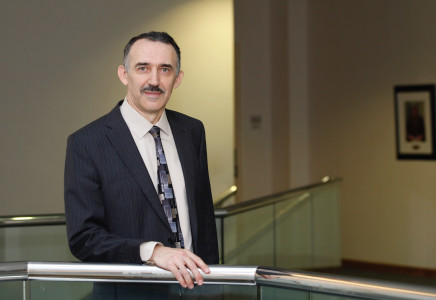 Andrei Seryi, Associate Director for Accelerator Operations, Research and Development, poses for a headshot wearing a dark blue suit with office halls in the background.