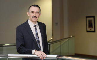 Andrei Seryi, Associate Director for Accelerator Operations, Research and Development, poses for a headshot wearing a dark blue suit with office halls in the background.