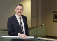 Andrei Seryi, Associate Director for Accelerator Operations, Research and Development, poses for a headshot wearing a dark blue suit with office halls in the background.