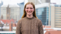 A woman poses in front of buildings. 