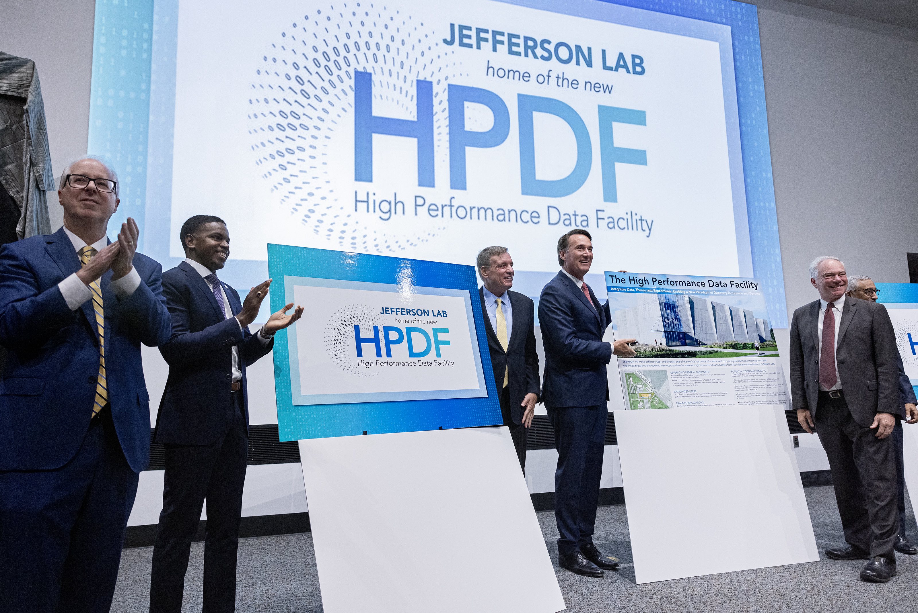 Honored speakers unveil the new High Performance Data Facility logo, including (l-r) Jefferson Lab Director Stuart Henderson, Newport News Mayor Phillip Jones, Virginia U.S. Senator Mark R. Warner, Commonwealth of Virginia Governor Glenn Youngkin, Virginia U.S. Senator Tim Kaine and U.S. Representative Bobby Scott.